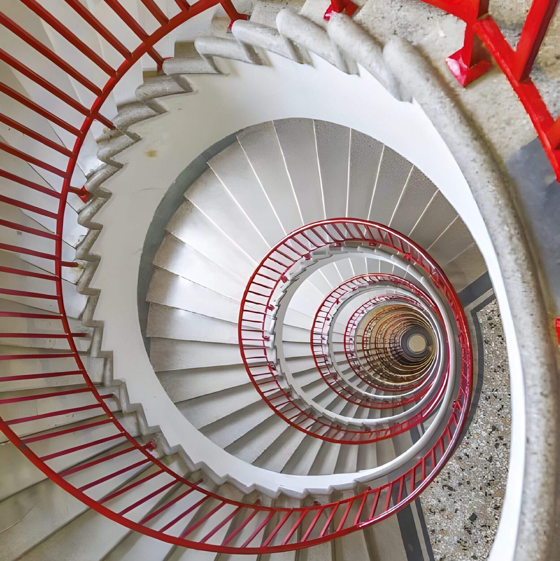 Escalier en colimaçon aux marches blanches et à la rampe rouge vif, vu d'en haut, formant un motif géométrique et tourbillonnant sur plusieurs étages.