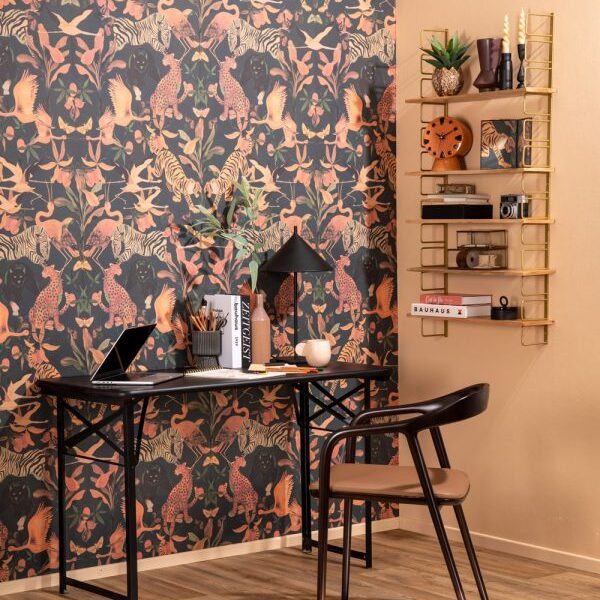 Un espace de travail moderne composé d'un bureau noir, d'une chaise, d'un ordinateur portable et d'une lampe de bureau est adossé à un mur recouvert d'un papier peint coloré sur le thème de la jungle. Une étagère murale dorée accueille des objets de décoration et des livres. Le sol est en bois clair.